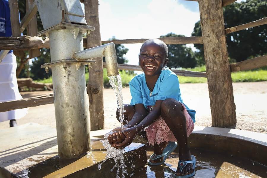 Boy from Uganda smiles next to water pump