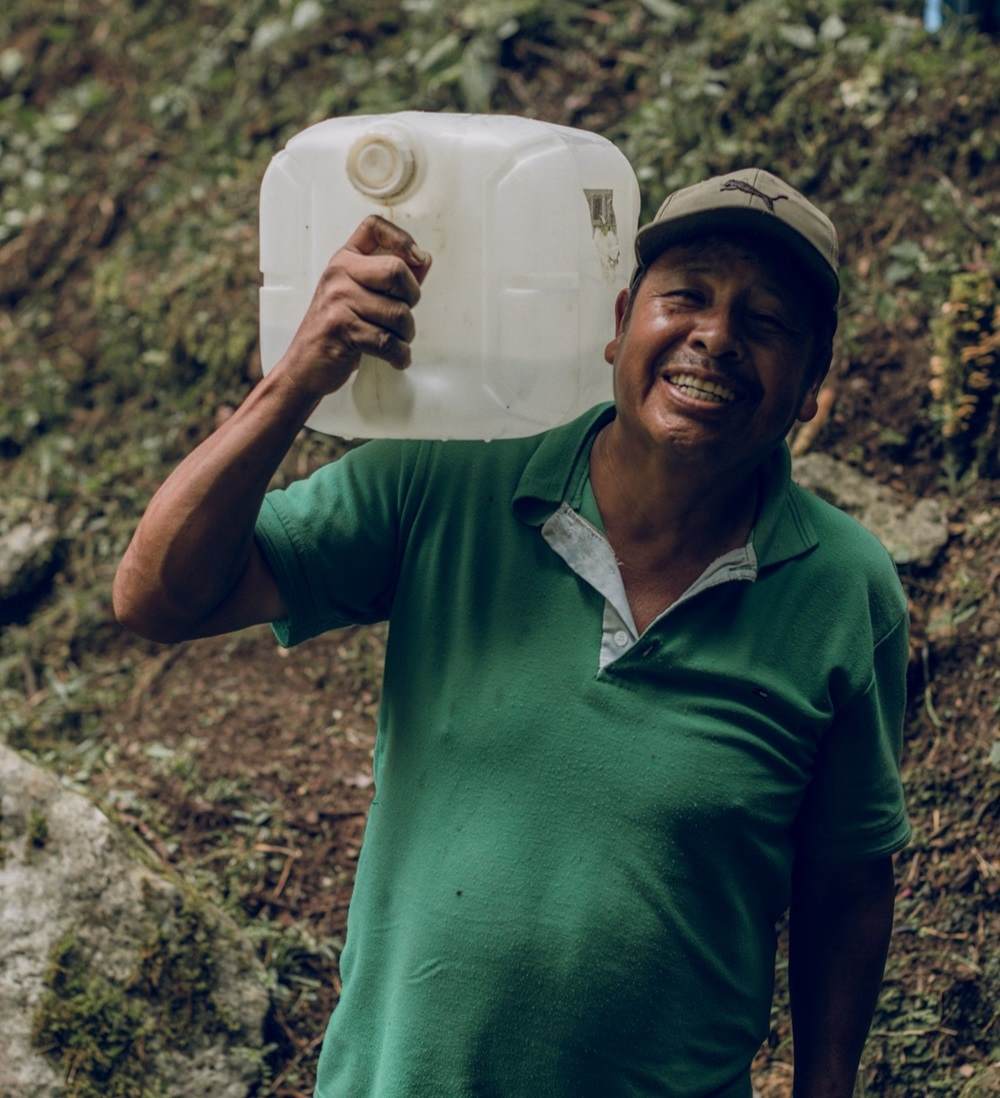 Indigenous man holds water collection bin for Fondo para la Paz
